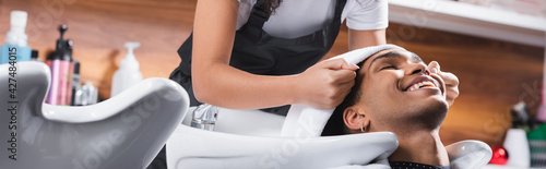 Hairdresser holding towel near head of smiling african american client and sink, banner