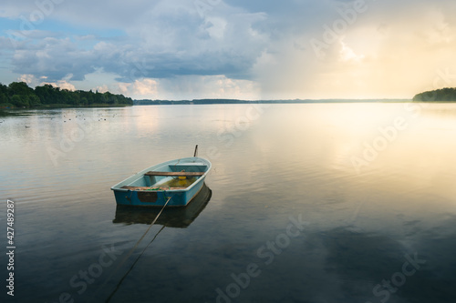 Wooden boat floating on the shore of a lake in Elk in the Mazury province of Poland. A storm comes in the background, as the sun disappears, calm before the storm.