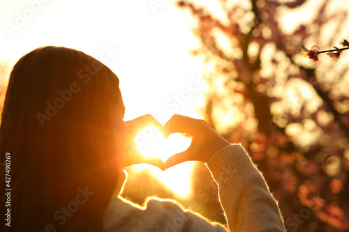 Woman hands making heart shape at sunset photo