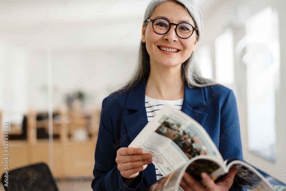 Φωτογραφία The smiling Asian woman leafing through magazine and looking at camera in the of