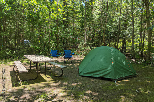 Clean campsite with green tent, picnic table and foldable camping chairs in front of the fire pit. Camping, hiking, vacation concept. Northern Ontario, Canada.