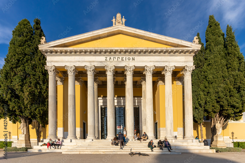 Obraz premium Athens, Attica, Greece. Facade of the famous neo classical building Zappeion Hall in the center of Athens city. People are sitting on the stairs relaxing under the bright sun