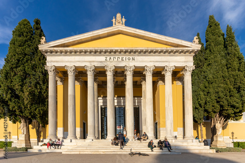 Athens, Attica, Greece. Facade of the famous neo classical building Zappeion Hall in the center of Athens city. People are sitting on the stairs relaxing under the bright sun