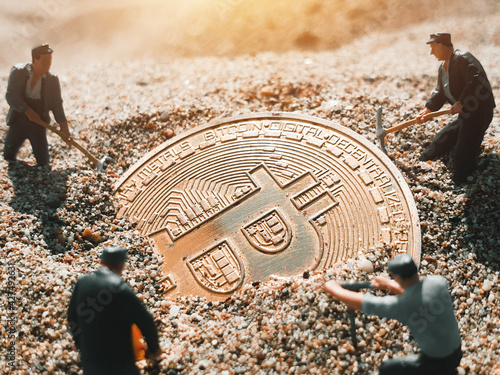 Macro miner figurines digging ground to uncover big shiny bitcoin. Cryptocurrency, blockchain and mining or trading concept. photo