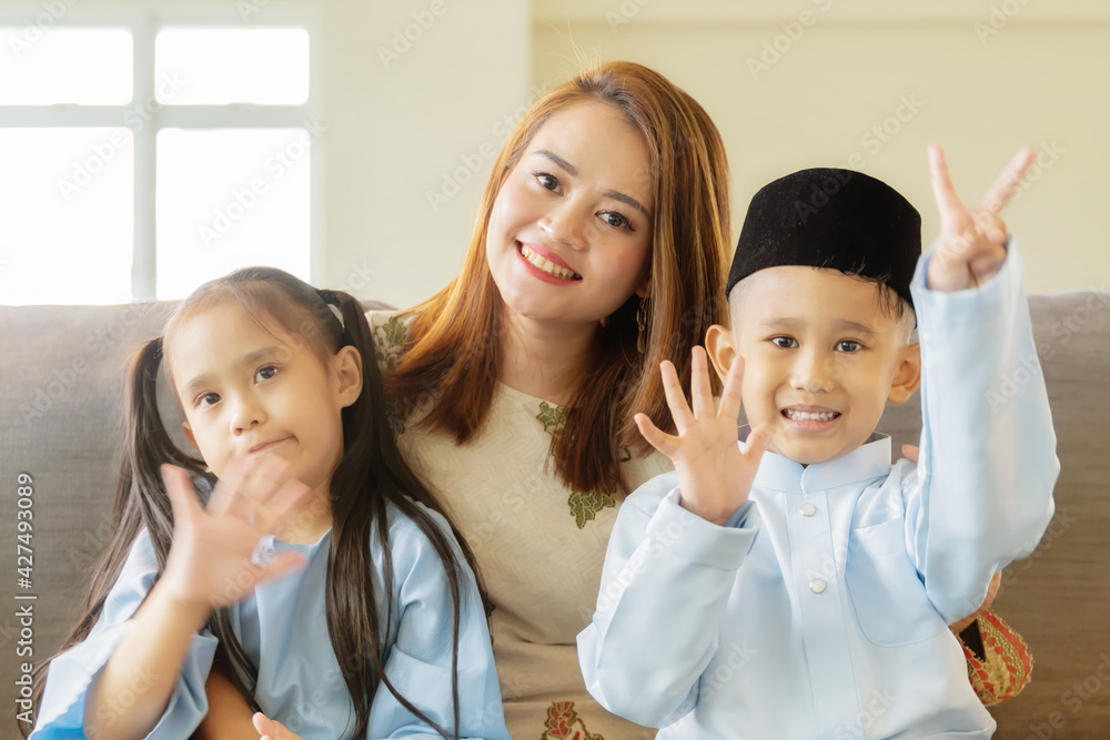 Eid Mubarak celebration moment, siblings at the sofa smiling to the camera Eid Mubarak celebration moment, siblings at the sofa smiling to the camera
