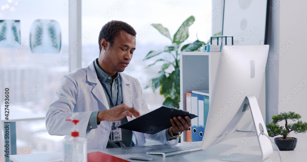 Naklejka premium African American Young Professional Doctor Talking to Patient using Computer for Remote Communication Advising Medicine and Discussing Disease.