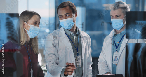 Professional medial colleagues in surgical masks negotiating in modern private business office about coronavirus vaccination. Cooperation.