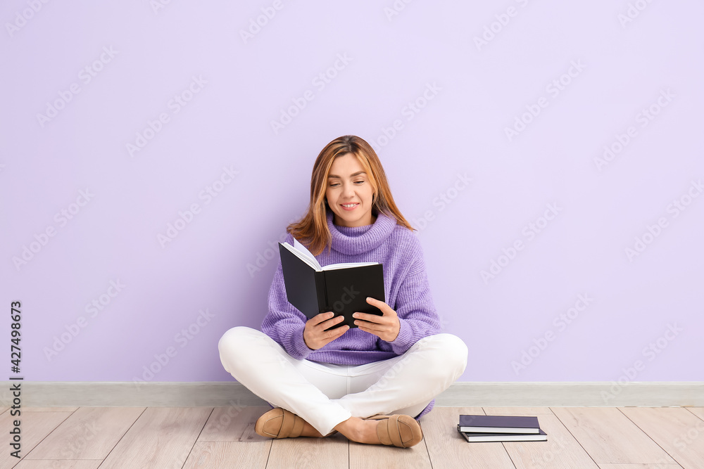 Woman reading books while sitting near color wall Woman reading books while sitting near color wall