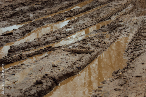 mud on the muddy road. tracks from the wheels of passing cars in the wet, softened ground. the road is difficult for transport to pass. puddles in the pits of a country dirt road