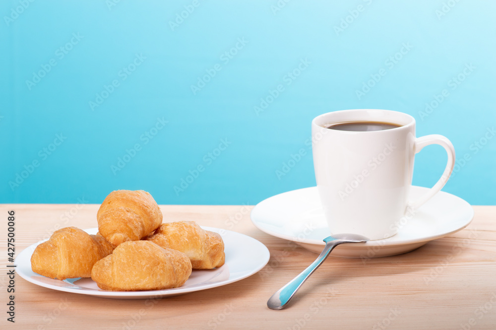 delicious coffee with croissant on wooden table and blue background delicious coffee with croissant on wooden table and blue background