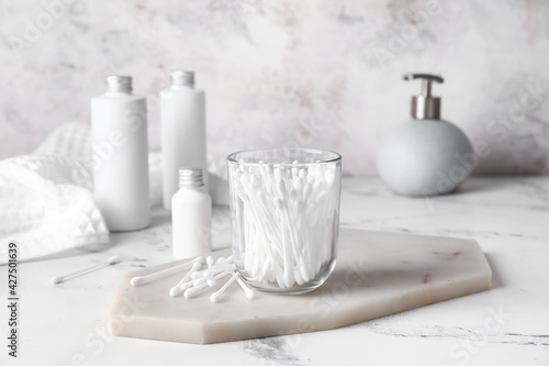 Glass with cotton swabs and cosmetic products on table in bathroom