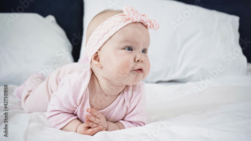 infant baby girl lying on bed while looking away.