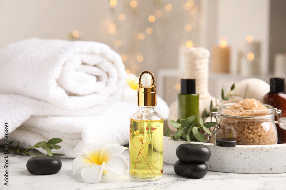 Beautiful spa composition with essential oil and plumeria flower on white marble table against blurred lights