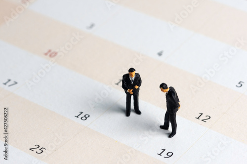 Selective focus miniature businessman standing on calendar checking schedule.