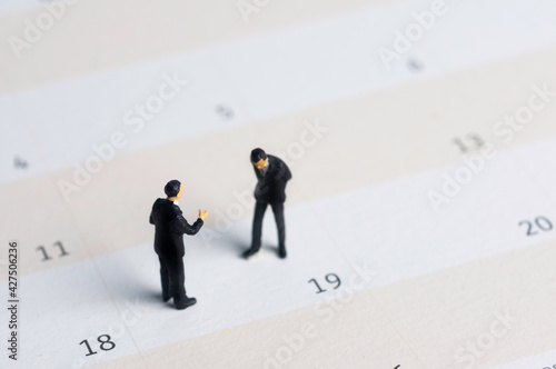Selective focus miniature businessman standing on calendar checking schedule.