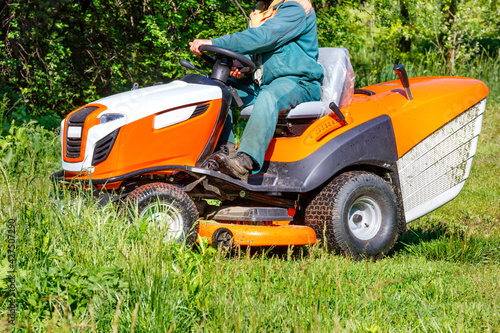 A gardener mows a green meadow with a tractor lawn mower.