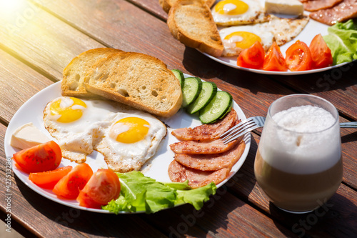 Continental breakfast set of eggs, ham, vegetables and cheese. Bread and coffee on a wooden table. Breakfast for two outside on a sunny summer day.