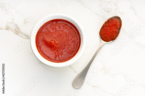 Fresh tomato sauce on bowl and spoon on white marble table