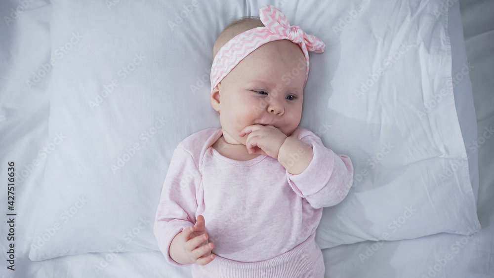 top view of baby with headband lying on bed and sucking fingers. top view of baby with headband lying on bed and sucking fingers.