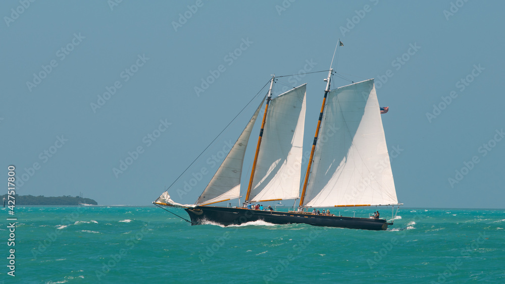 Naklejka premium Sailboat or Sail yacht with American flag. Private cruise tour. Summer vacations on ocean or Gulf of Mexico Florida. Yachting sport. Turquoise ocean color. Beautiful seascape.