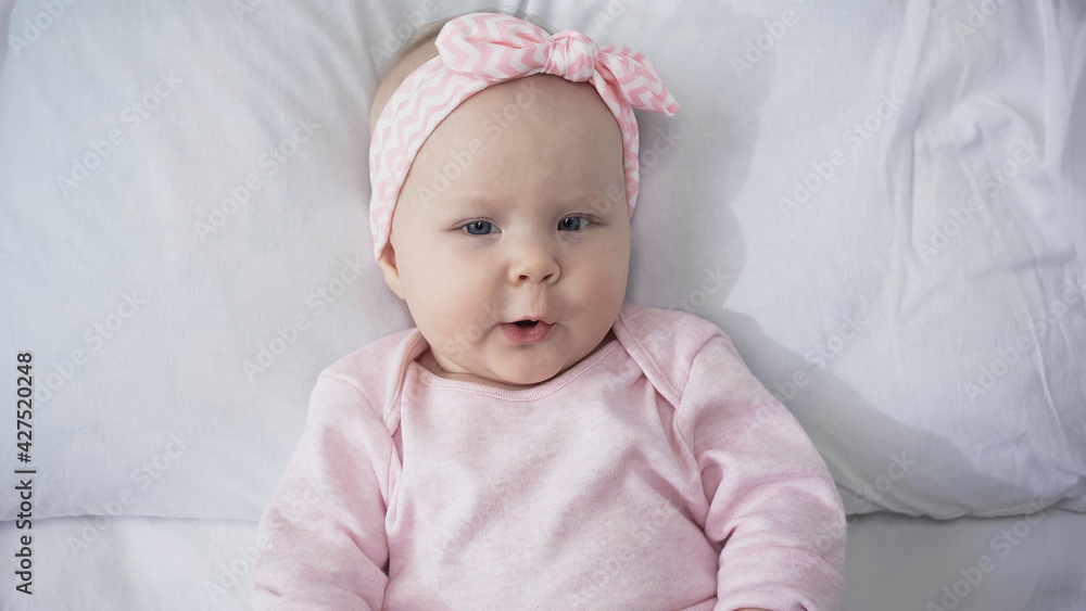 top view of infant girl in headband looking at camera while lying in bed. top view of infant girl in headband looking at camera while lying in bed.