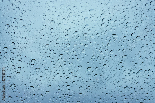 Wet windshield, taken from inside the car.Rain falls on the surface of a car glass window with a gray background. Natural patterns of raindrops on the windshield. Water drops wallpaper. 