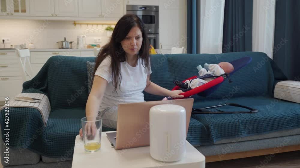Mother trying to work on laptop at home in the kitchen with baby next to her. High quality 4k footage Mother trying to work on laptop at home in the kitchen with baby next to her. High quality 4k footage