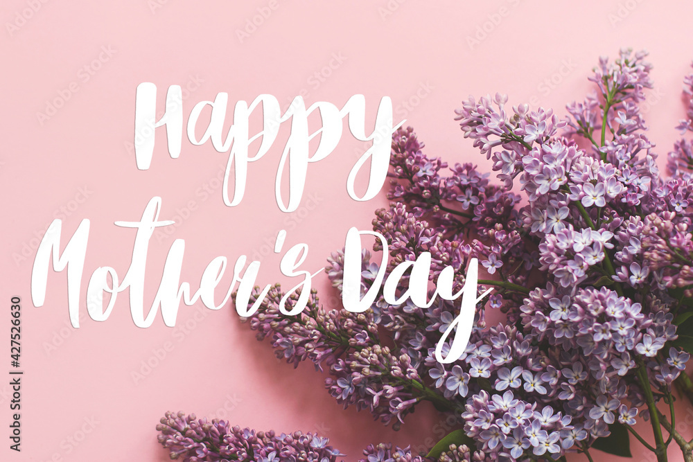 Fototapeta premium Happy mother's day. Happy mother's day text and lilac flowers on pink paper. Stylish floral greeting card. Handwritten lettering on purple lilac branch on pink. Mothers day