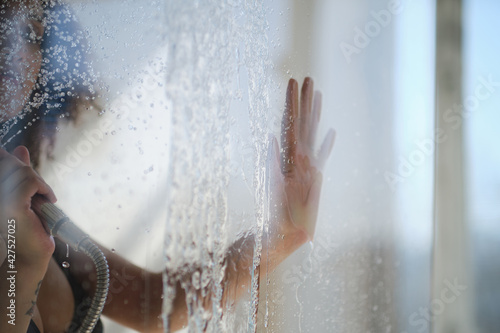 female hand on the glass door of the shower stall. Sensual portrait of young woman taking a shower. Defocused female looks through the glass of the shower stall.