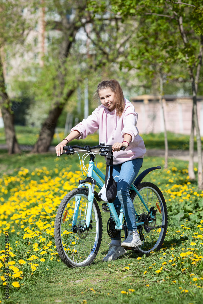 Portrait of teenager Caucasian girl standing with bicycle in spring park with yellow flowers Portrait of teenager Caucasian girl standing with bicycle in spring park with yellow flowers