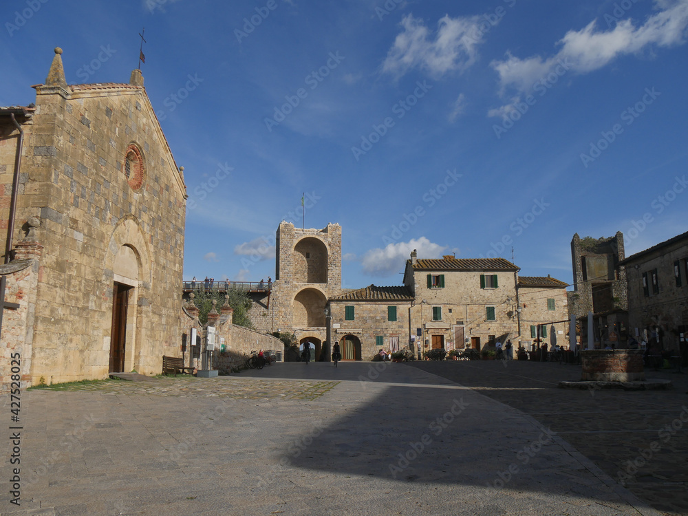 Piazza Roma in Monteriggioni with the church of Santa Maria Assunta and a well and the walls with Porta Romea in the background