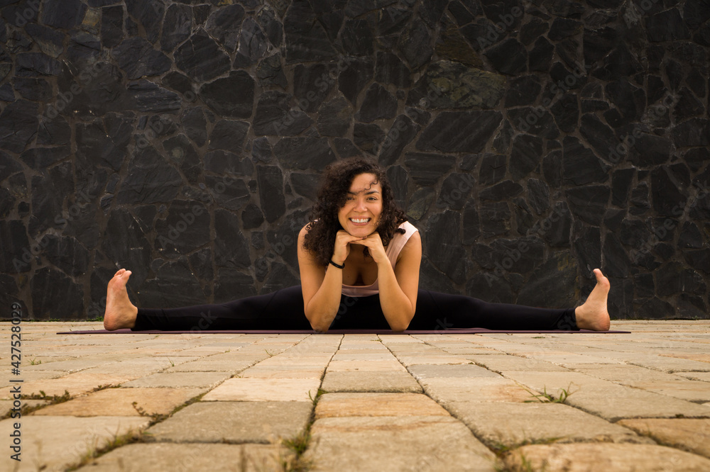 Beautiful young woman with curly hair sitting on split and smiling. Yoga postures