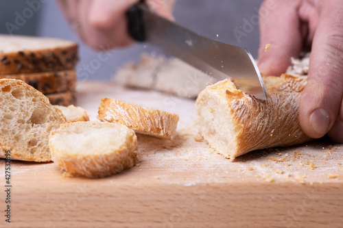 Male hands cutting fresh baguette on the wooden table