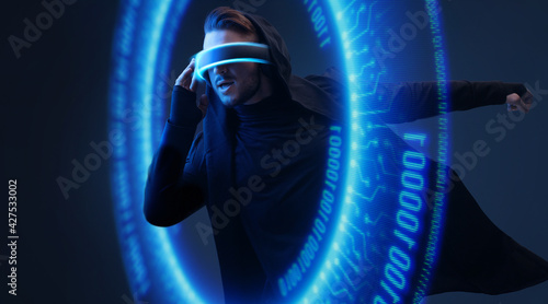 Man on dark virtual reality background. Guy using VR helmet. Augmented reality, future technology, game concept. Blue neon light. Futuristic holographic interface to display data. © KDdesignphoto