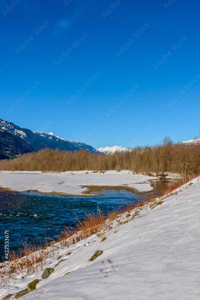 Majestic mountain river in winter over snow mountains and blue sky in Vancouver, Canada.