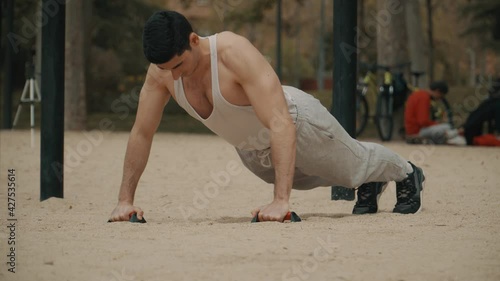 hombre haciendo flexiones en el parque, hombre de pelo negro haciendo deporte al aire libre, hombre musculoso en camiseta de tirantes  blanca haciendo ejercicio photo