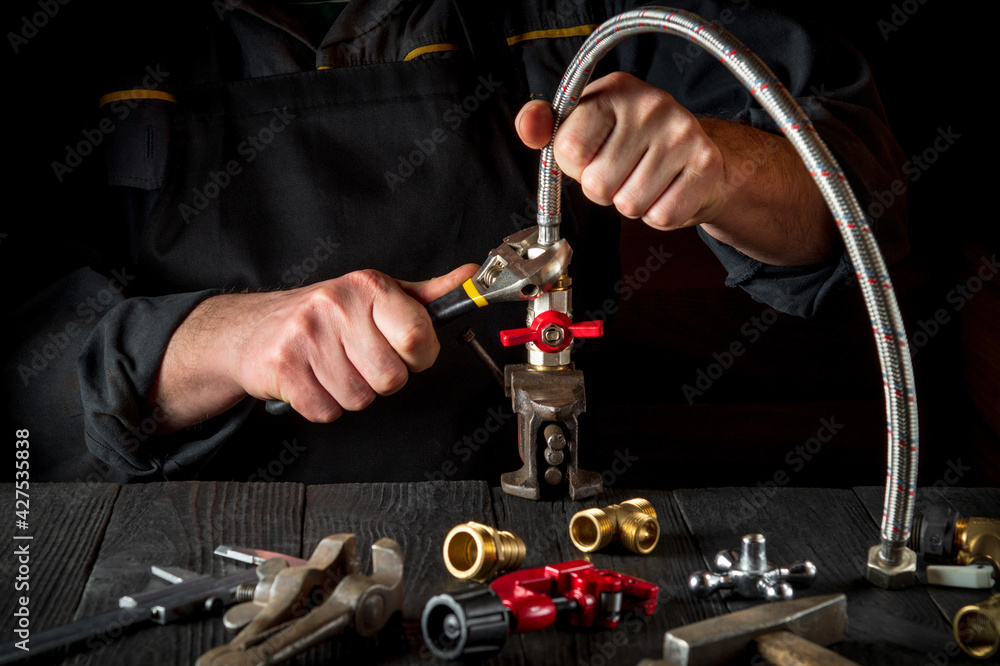 The plumber connects the brass fittings to the faucet with an adjustable wrench. Close-up of a foreman is hands while working in a workshop The plumber connects the brass fittings to the faucet with an adjustable wrench. Close-up of a foreman is hands while working in a workshop