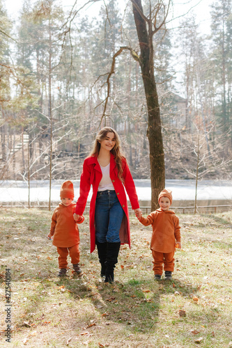 Happy young beautiful mother holds two little sons by the hands. Weekend walk in the spring forest. Children boys twins