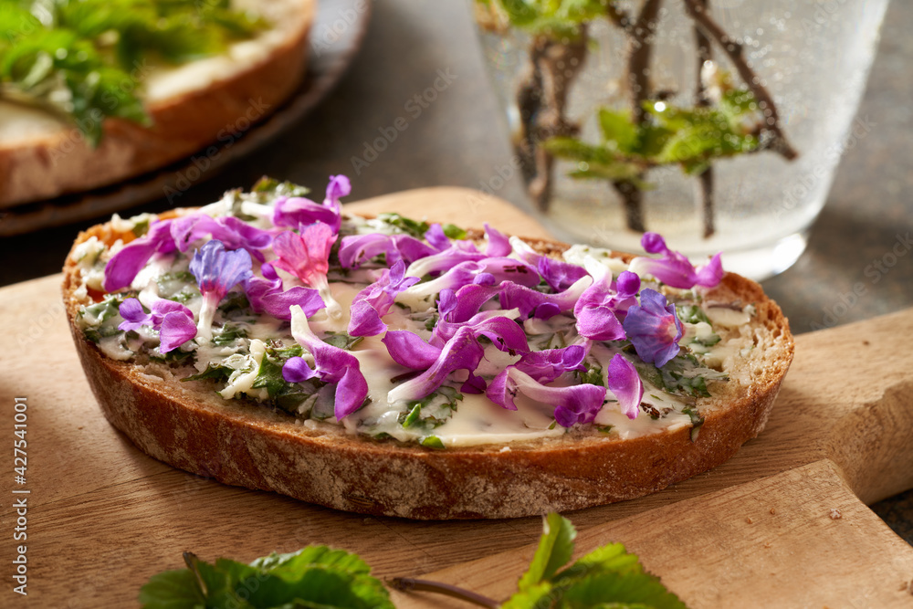 Slice of bread with spring wild edible plants - young ground elder leaves, purple dead-nettle and lungwort flowers