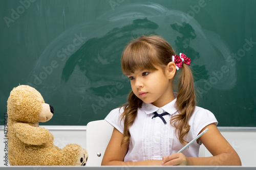 Cute girl sitting at desk with her teddy bear toy