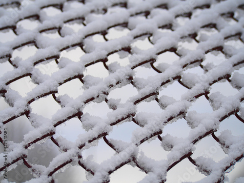 Snow-covered mesh. The lattice fence is covered with fresh snow. White background texture. Selective, soft focus.