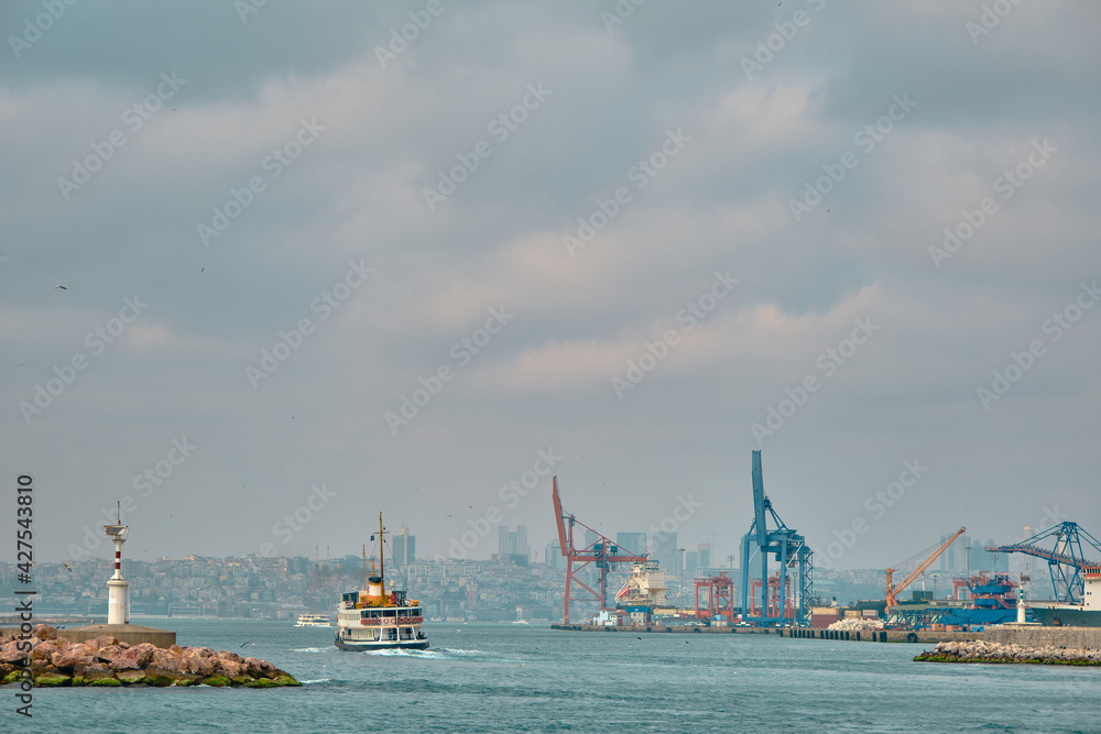 Turkey, istanbul 04.03.2021. Bosphorus of istanbul with pedestrian ferry and ship with haydarpasa port and harbor with marine cranes during overcast and rainy day on turquoise color sea of marmara