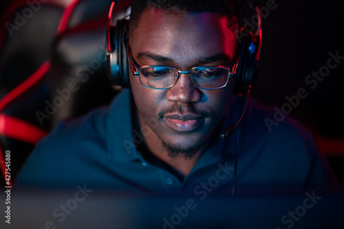 A close-up portrait of a handsome dark-skinned man wearing glasses and a headset in front of a computer photo