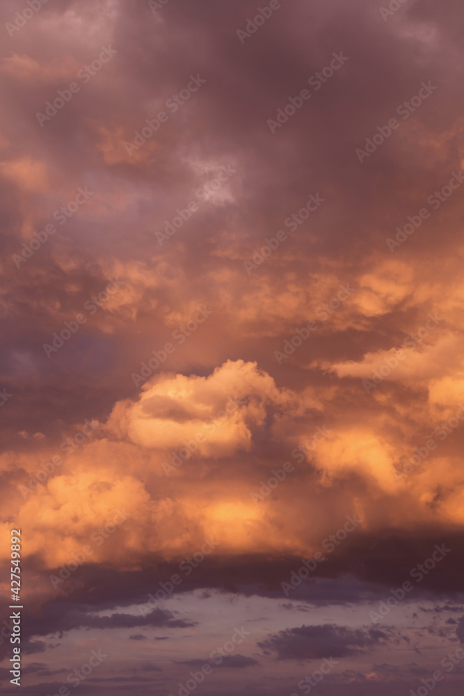 Epic sunset storm sky. Big cumulus thunderstorm clouds in red orange sunlight background texture