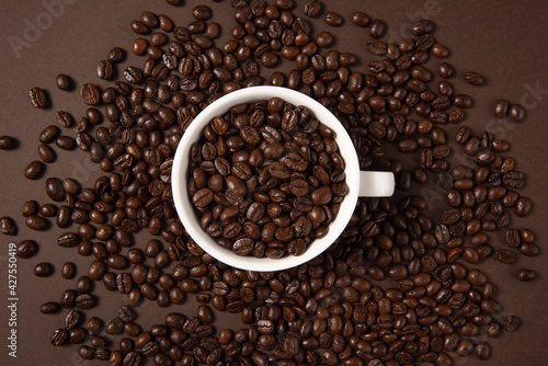 A cup of coffee wih coffee beans on brown background, top view
