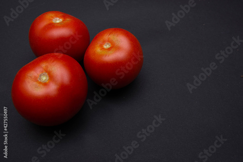 Zbliżenie na trzy czerwone dojrzałe pomidory na czarnym tle, miejsce na tekst