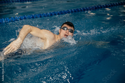 Caucasian athlete-swimmer crawls in the blue water. Portrait of a young male triathlete swimming in swimming goggles. Triathlon training concepts for triathletes