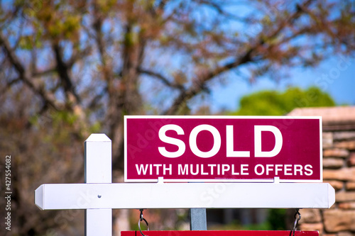 SOLD With Multiple Offers real estate sign near purchased house indicates hot seller's market in the desired neighborhood. Blurred outdoor background photo