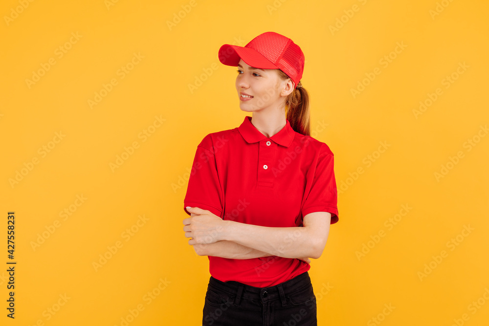 Smiling young woman courier wearing red uniform posing on yellow studio background Smiling young woman courier wearing red uniform posing on yellow studio background