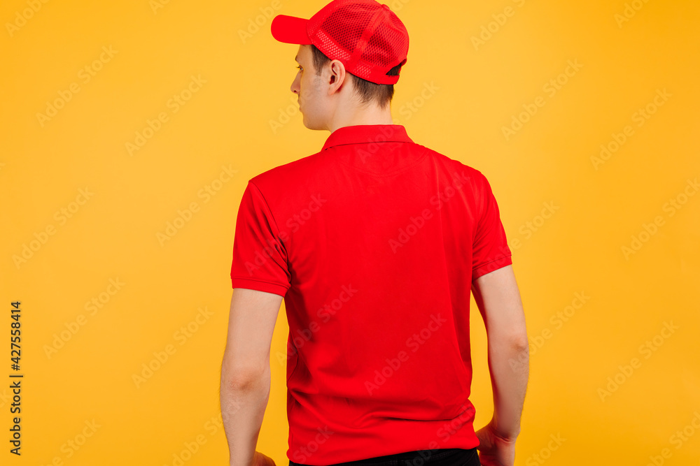 Rear view, courier wearing red uniform posing on yellow studio background Rear view, courier wearing red uniform posing on yellow studio background